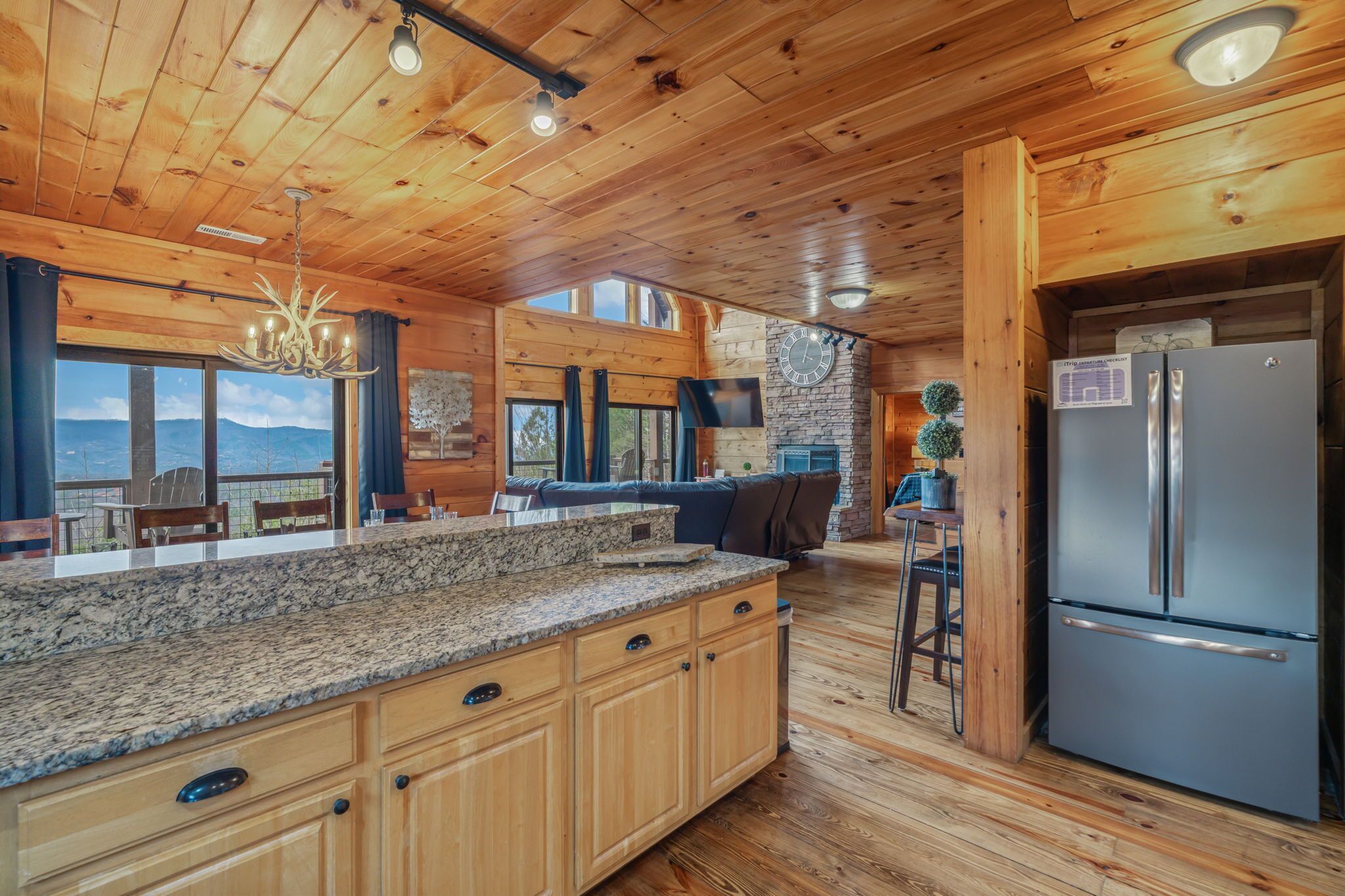 A wooden cabin interior with a kitchen, dining area, and a stone fireplace.