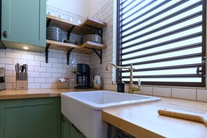 Una cocina con un lavamanos, estantes de madera y una ventana con persianas.