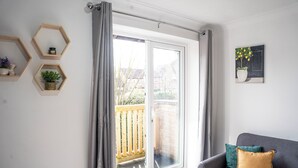 Ein Wohnzimmer mit grauem Sofa, einer Schiebetür zum Balkon und sechseckigen Regalen mit Pflanzen und einer Kerze.