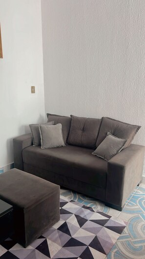 Ein dunkelbraunes Sofa mit vier Kissen, ein passendes Ottomanen und ein gemusterter Boden.