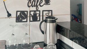 Keittiössä on kahvinkeitin, kahvikuppi ja seinällä oleva kyltti, jossa lukee: ”Cantinho Café”.