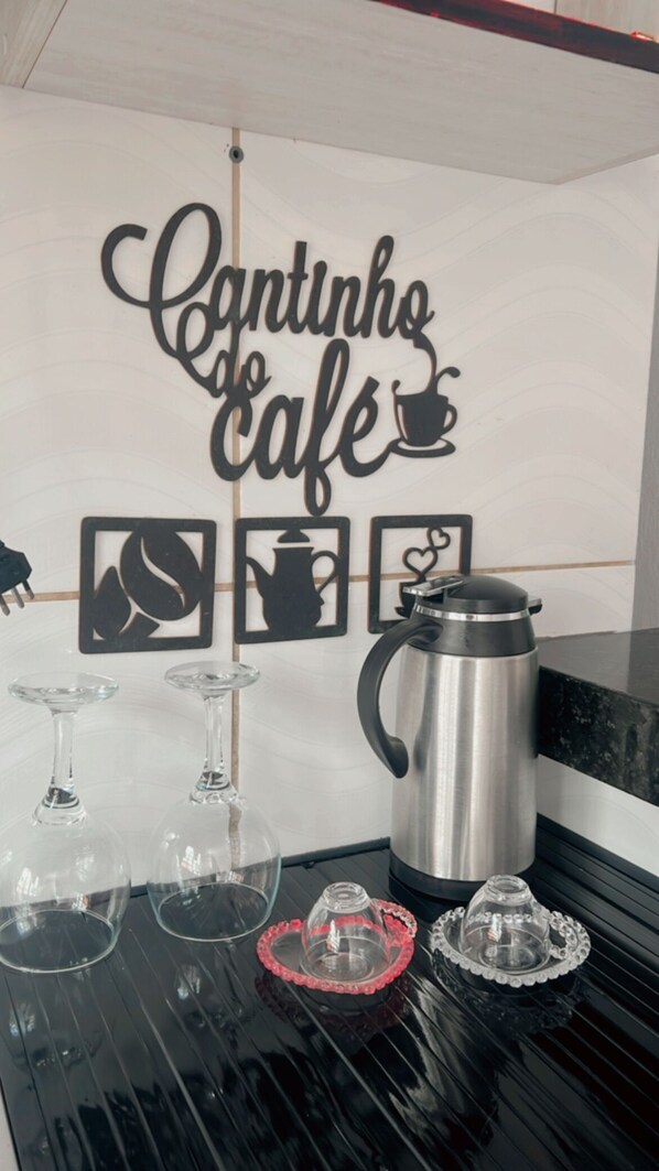 A kitchen counter with a coffee maker, two wine glasses, and a decorative sign that reads 'Caminhos Café'.
