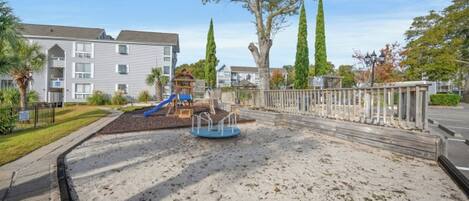A playground with a slide, a small play structure, and a sandy area.