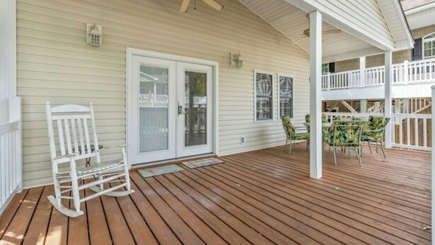 A covered wooden deck with a rocking chair, a glass door, and a ceiling fan. - 3 Bedroom House (7033) in Ocean Lakes Campground (Myrtle Beach)