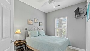 A bedroom with a bed, a nightstand, a lamp, a ceiling fan, and a window with blinds. - 3 Bedroom House (7033) in Ocean Lakes Campground (Myrtle Beach)