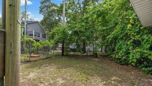 A backyard with a wooden fence, a house in the background, and a tree in the foreground. - 3 Bedroom House (7033) in Ocean Lakes Campground (Myrtle Beach)