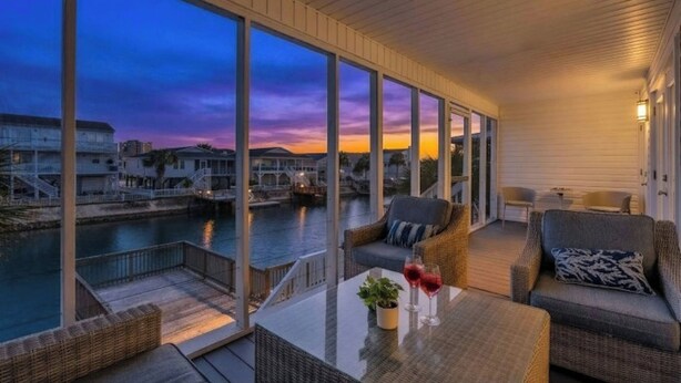 Un balcon spacieux offrant une vue sur le bord de l’eau, aménagé avec des fauteuils en osier et une table en verre.