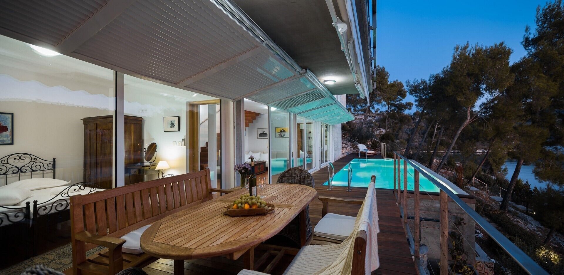 A poolside area with a wooden table and chairs, a bed, and a view of the pool.