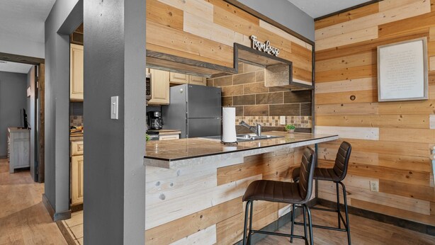 A modern kitchen with a wooden accent wall, a built-in island with bar stools, and a visible kitchen counter. - Hole-in-one Hideaway For 4 (Branson)