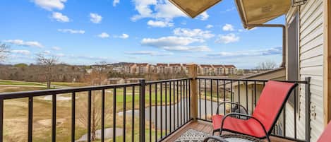 Un balcon donnant sur un quartier résidentiel, une chaise rouge et un tapis à motifs.