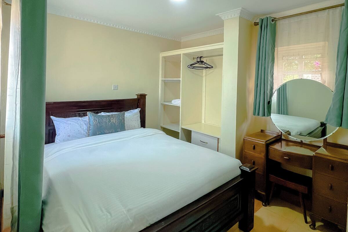 A bedroom with a bed, a dresser, a mirror, a wardrobe, and a ceiling light.