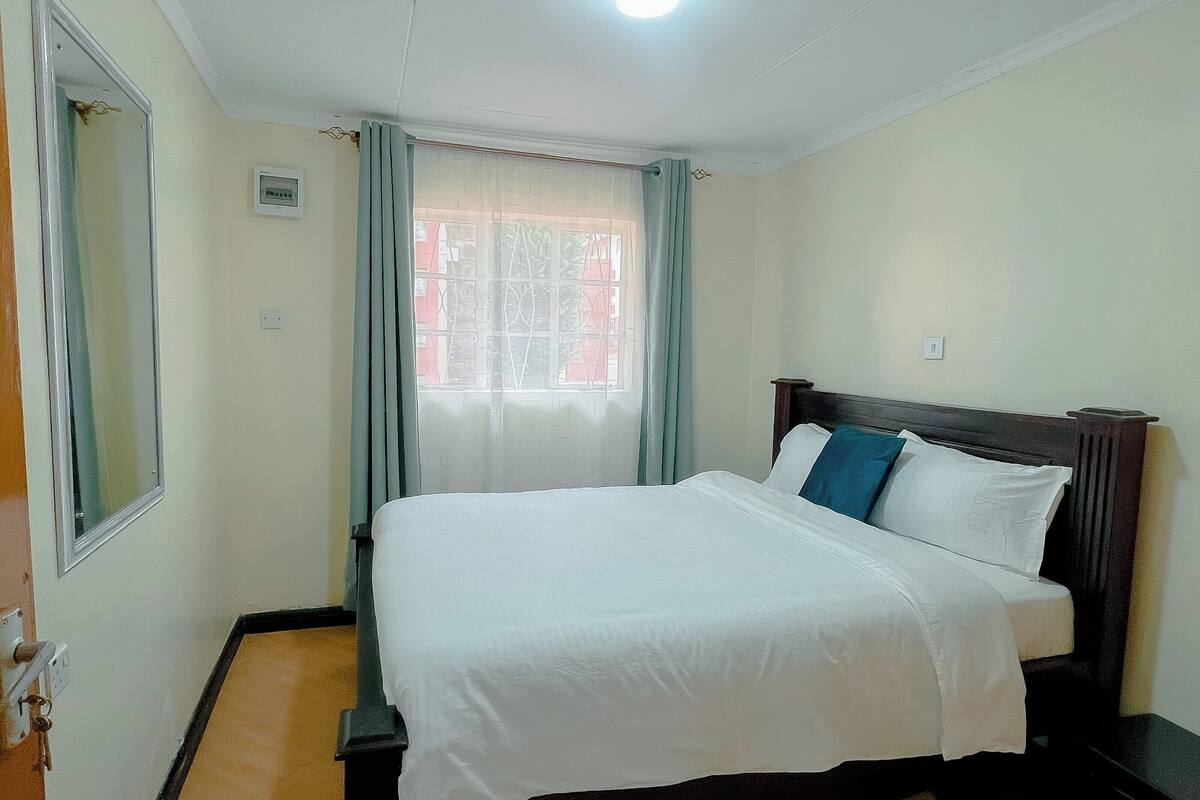 A bedroom with a bed, a window with curtains, a ceiling light, and a door.