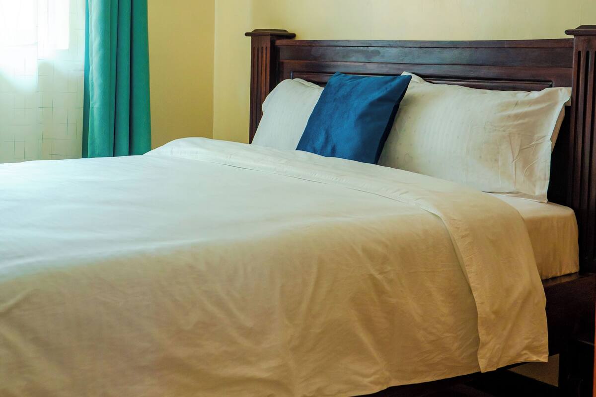A bed with white bedding, a wooden headboard, and a blue pillow.