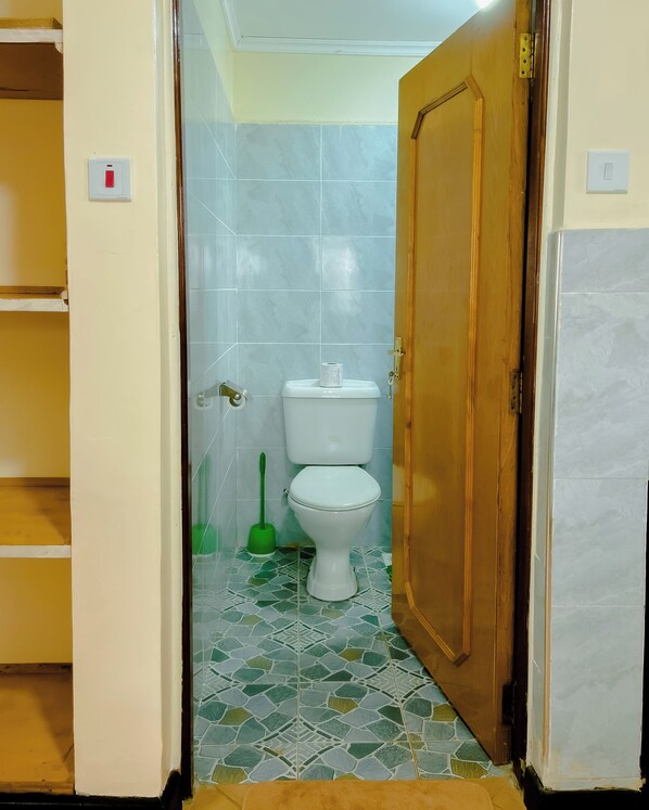 A bathroom with a toilet, a green broom, and a tiled floor.