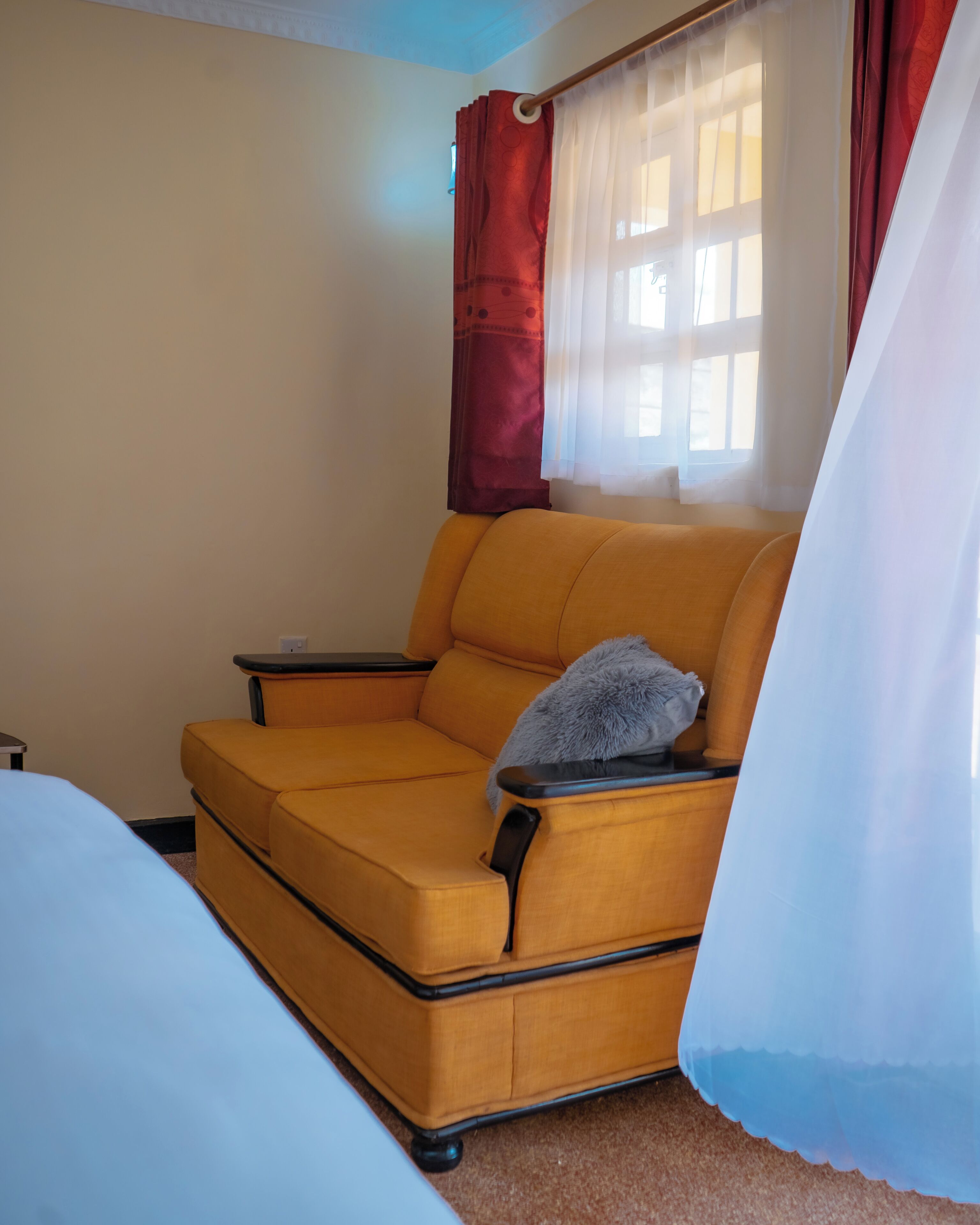 A room with a yellow sofa, a small table, a bed, and a window with curtains.