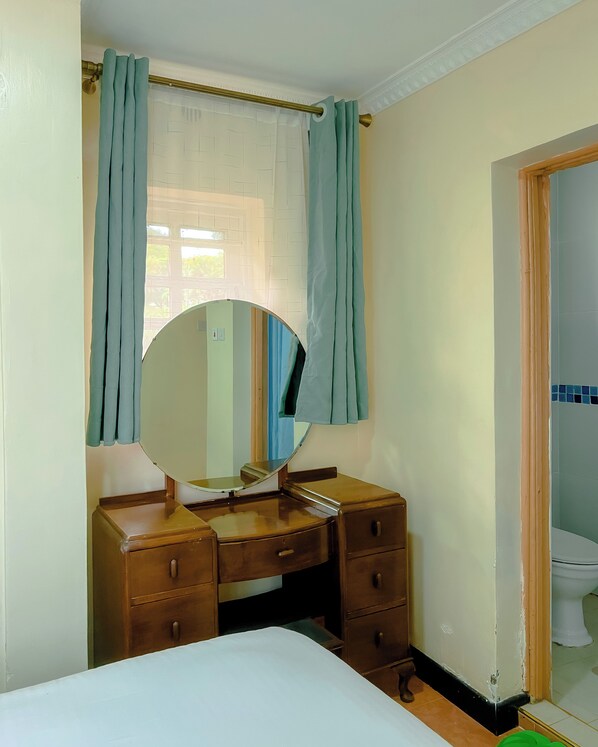 Une chambre à coucher avec un lit, une commode en bois, un miroir rond et une fenêtre avec des rideaux.