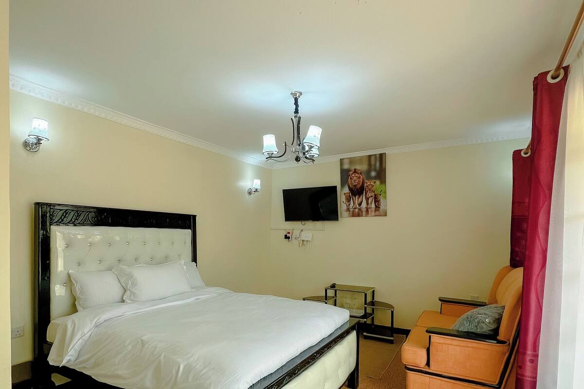 A bedroom with a bed, a chair, a television, and a chandelier.