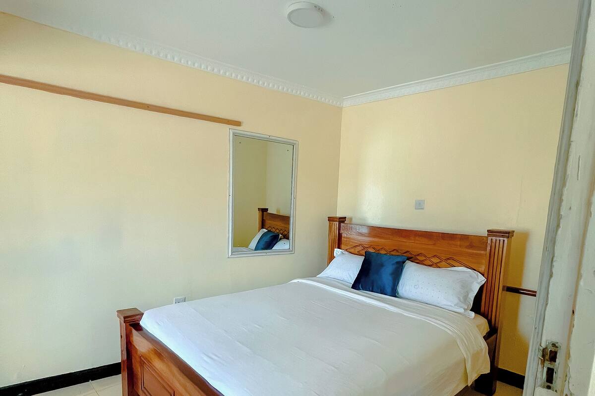 A bedroom with a wooden bed, a bedside table, a mirror, and a door.
