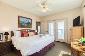 A bedroom with a large bed, a ceiling fan, a painting, a television, and a door leading to a balcony. - The Shoreline Social - Front Row Beach Home, Cheers! (Surfside Beach)