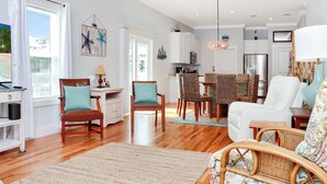 A spacious living area with a dining table, chairs, and a kitchen in the background. - ☀️ Rhapsody in Blues - 2 Decks - Steps to the Beach - Pet Friendly 🌴 (Mexico Beach)