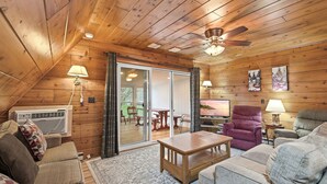 Ett mysigt rum med träväggar, en takfläkt, ett stort fönster och en skjutdörr i glas som leder ut till ett utomhusområde.