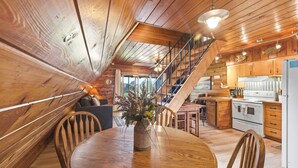 A wooden interior with a dining table, chairs, a kitchen area, and a staircase.