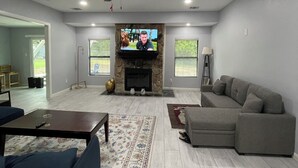 Ein geräumiges Wohnzimmer mit Kamin, Deckenventilator und einem großen, grauen Ecksofa.
