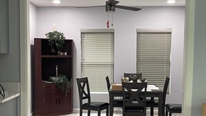 Ein Essbereich mit Tisch, Stühlen, Deckenventilator und Bücherregal.