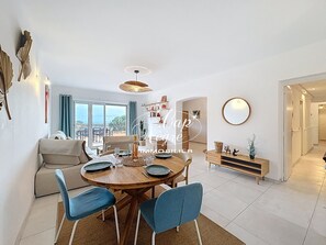 A dining area with a round table, blue chairs, a wooden cabinet, and a view through a glass door. - Elegant family villa with sea view for 4 people at La Fossette (Le Lavandou)