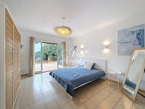 Une chambre à coucher avec un lit, un luminaire au plafond, une porte-fenêtre coulissante et un tableau au mur.