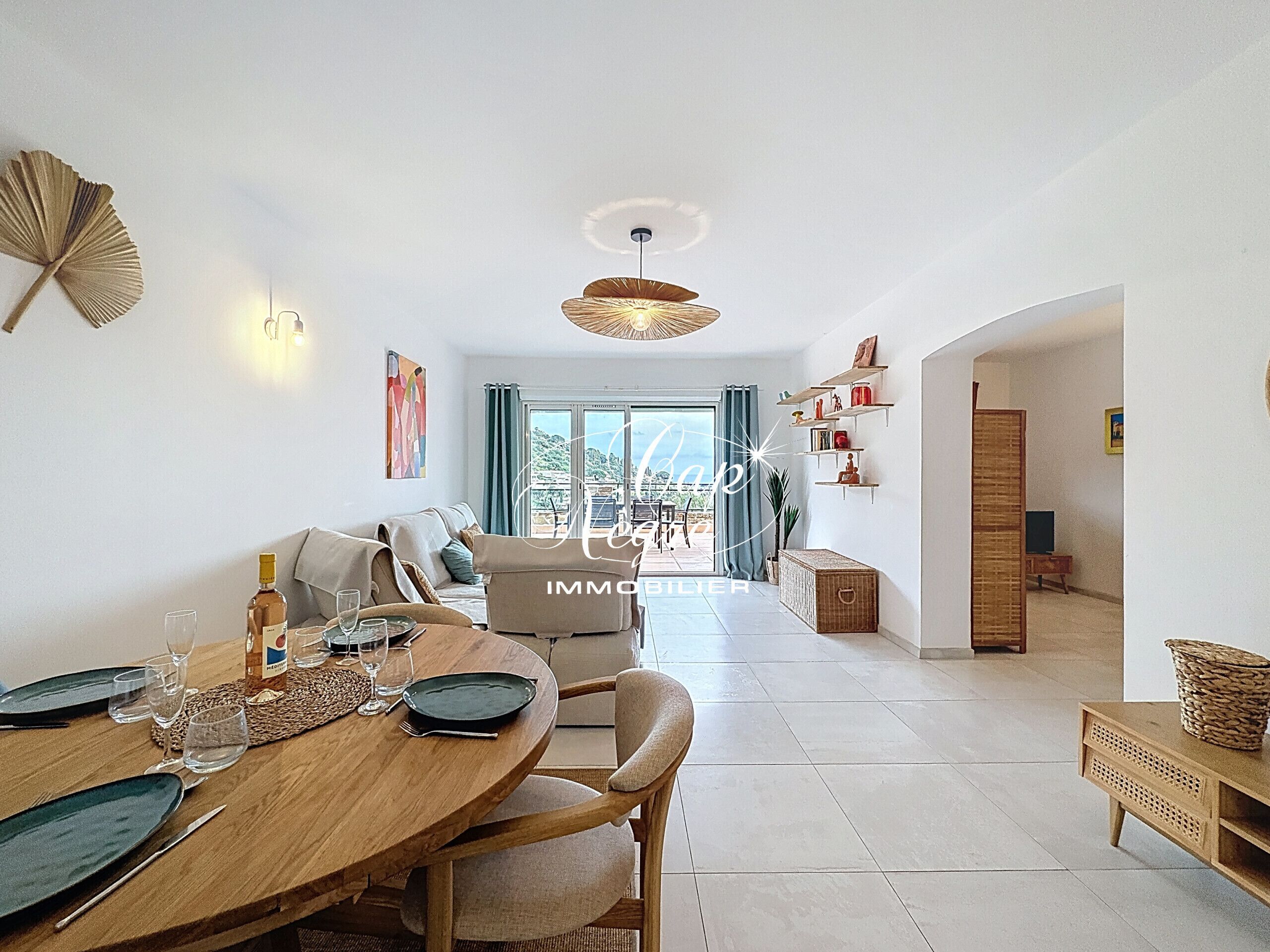 A dining area with a wooden table set for two, a sofa, and a view of the outdoors.