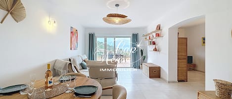 A dining area with a wooden table set for two, a sofa, and a view of the outdoors.