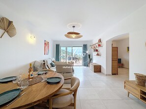 Un coin repas avec une table en bois dressée pour deux personnes, un canapé et une vue sur l’extérieur.