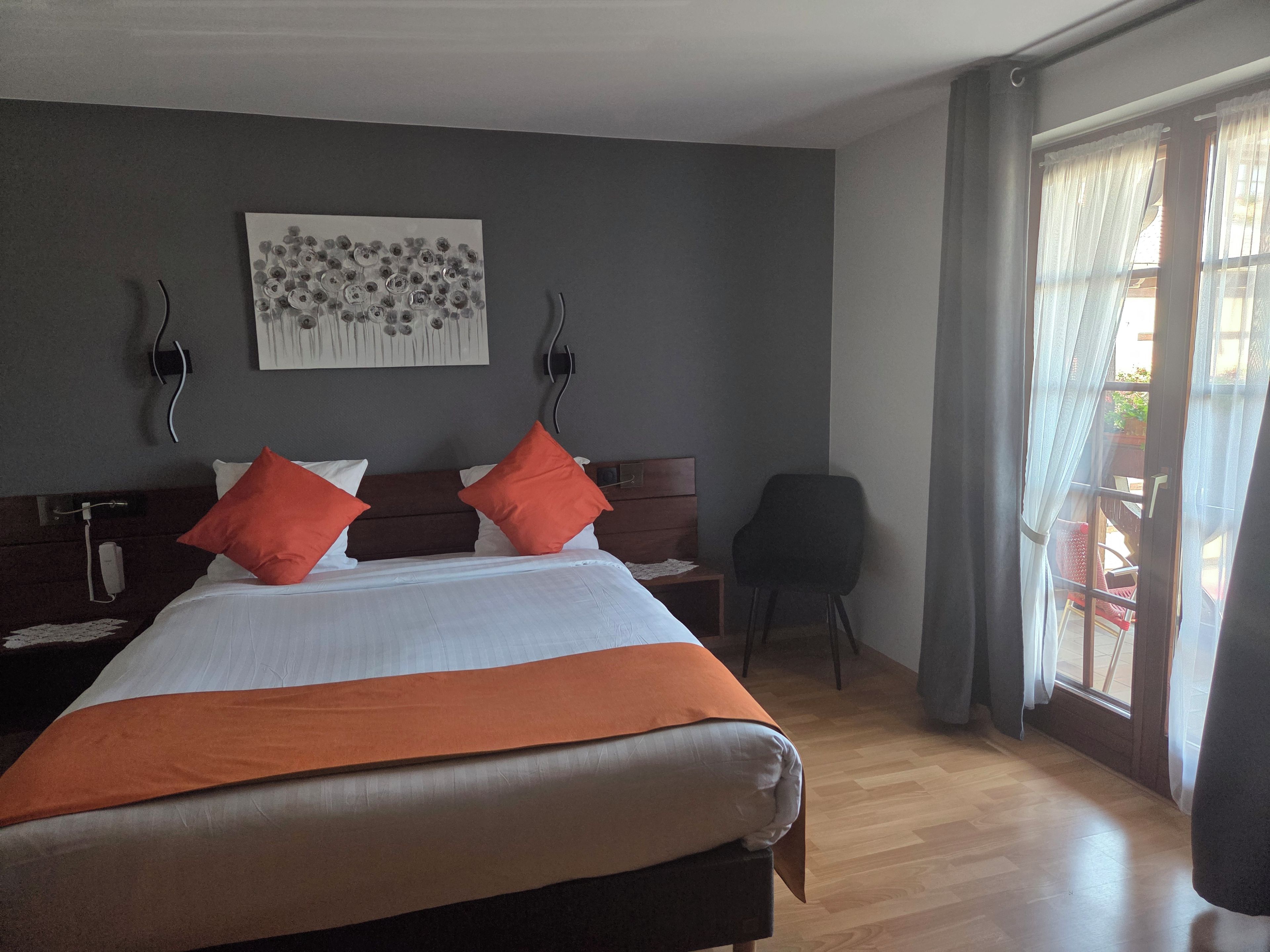 Habitación de hotel con cama, una silla, una mesita de noche, teléfono en la pared y una ventana con cortinas.