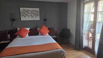 Habitación de hotel con cama, una silla, una mesita de noche, teléfono en la pared y una ventana con cortinas.