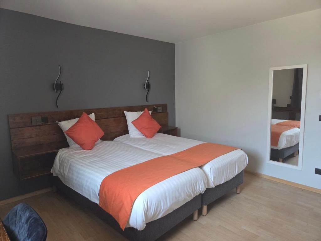 Een tweepersoonsbed met een houten hoofdbord, twee kussens en een oranje dekbedovertrek.