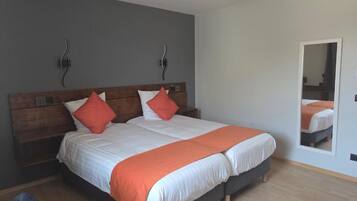 Een tweepersoonsbed met een houten hoofdbord, twee kussens en een oranje dekbedovertrek.