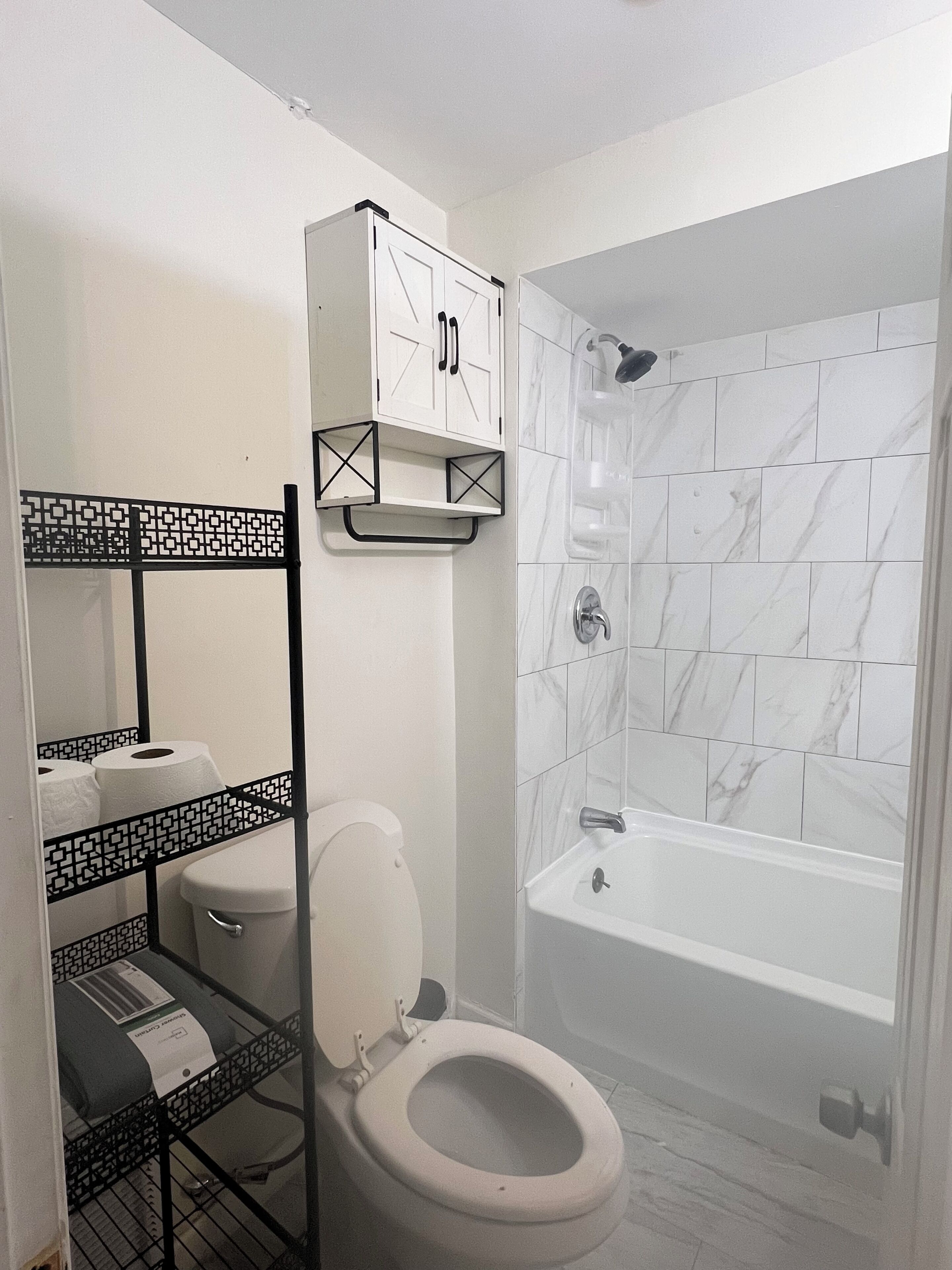 Un baño con inodoro, lavabo, ducha y pared de azulejos blancos.