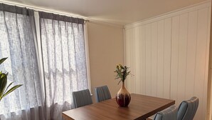 Un coin repas avec une table en bois, des chaises bleues, un vase de fleurs et un mur blanc avec des lambris.