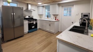 Une cuisine moderne dotée d’un réfrigérateur en acier inoxydable, d’une cuisinière à gaz, de meubles blancs et d’un plan de travail en marbre.