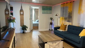 Un salon avec un canapé, une table basse et une lampe. Une porte donne accès à une autre pièce.