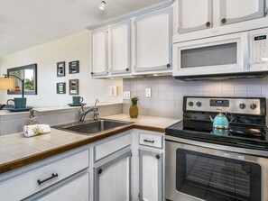 A kitchen with white cabinets, a stainless steel stove, a microwave, and a sink. - Kona Alii 609 - Ocean View Kona Condo | Walk to Beach & Town | AC (Kailua Kona)