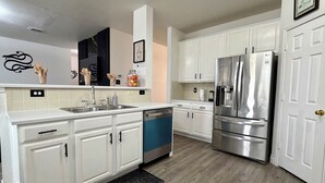 A modern kitchen with white cabinets, stainless steel appliances, and a black backsplash. - Big Beautiful BOLD (Grand Prairie)