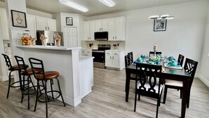 A modern kitchen with white cabinets, a central island, bar stools, and a dining table with chairs. - Big Beautiful BOLD (Grand Prairie)