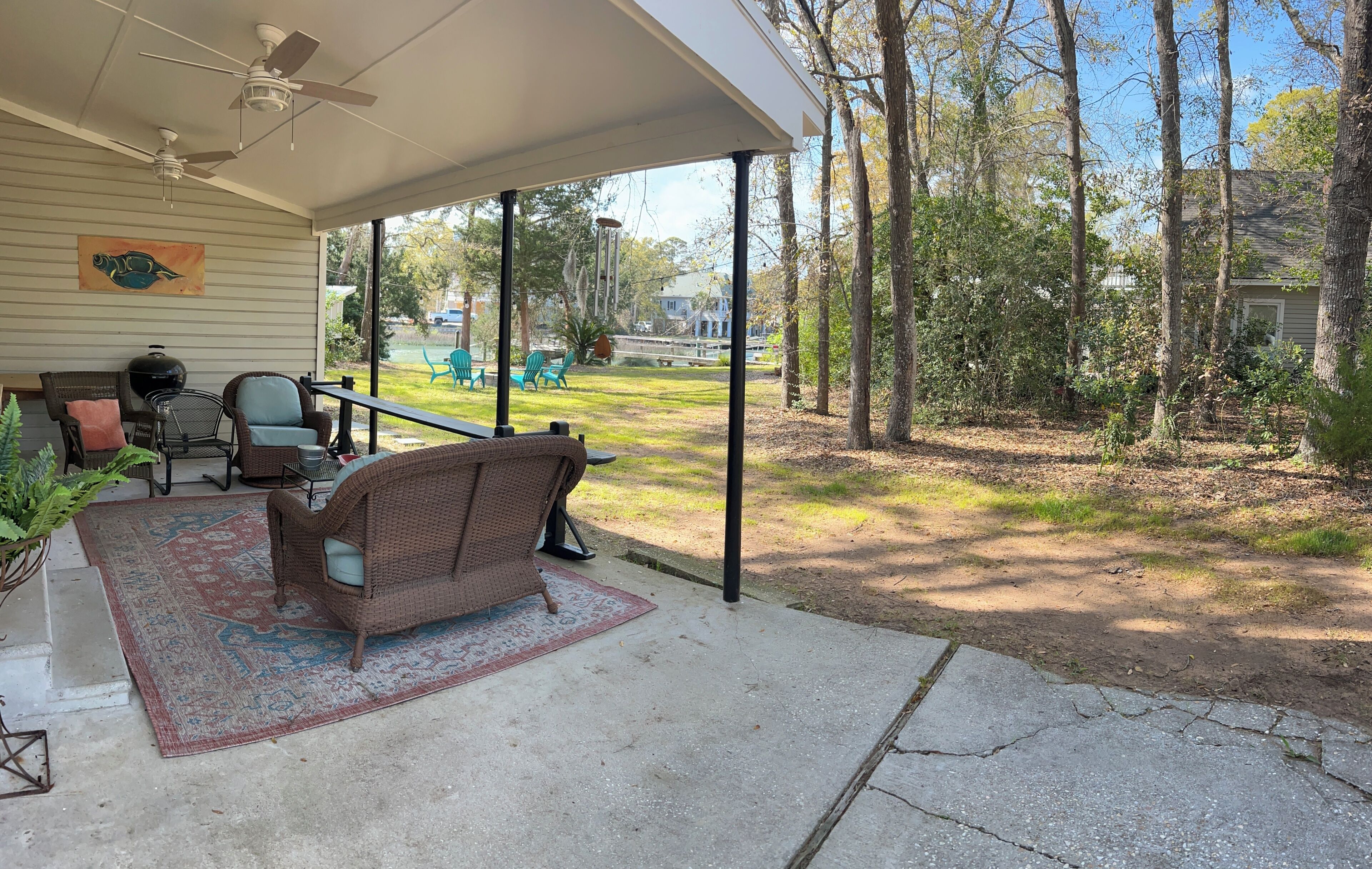 A covered patio with wicker furniture, a ceiling fan, and a view of a grassy yard.