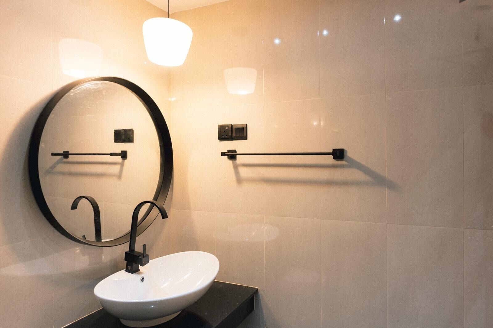 Une salle de bain moderne avec un miroir rond, un lavabo blanc et deux porte-serviettes.