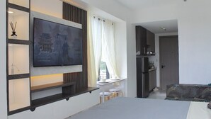 A modern hotel room with a large flat-screen TV mounted on the wall, a bed, a sofa, a small table with stools, and a wardrobe. - Pure Simplicity: Sip Coffee Overlooking the Glittering City (Cebu City)