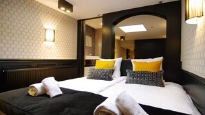 Une chambre d’hôtel avec un lit, deux oreillers, une serviette, un miroir et un mur orné d’un motif géométrique.