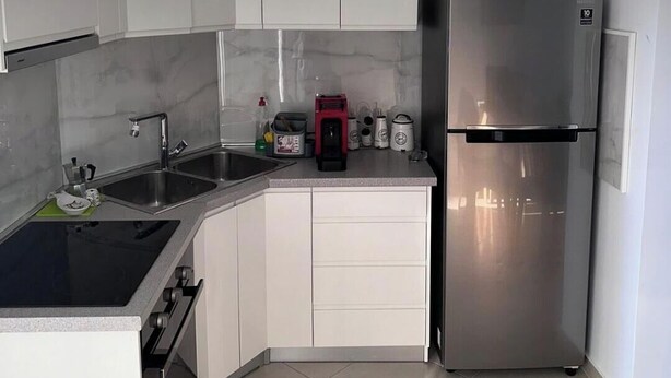 Eine moderne K üche mit weißen Schränken, einem Edelstahl-Kühlschrank, einem eingebauten Kochfeld und einer Spüle.