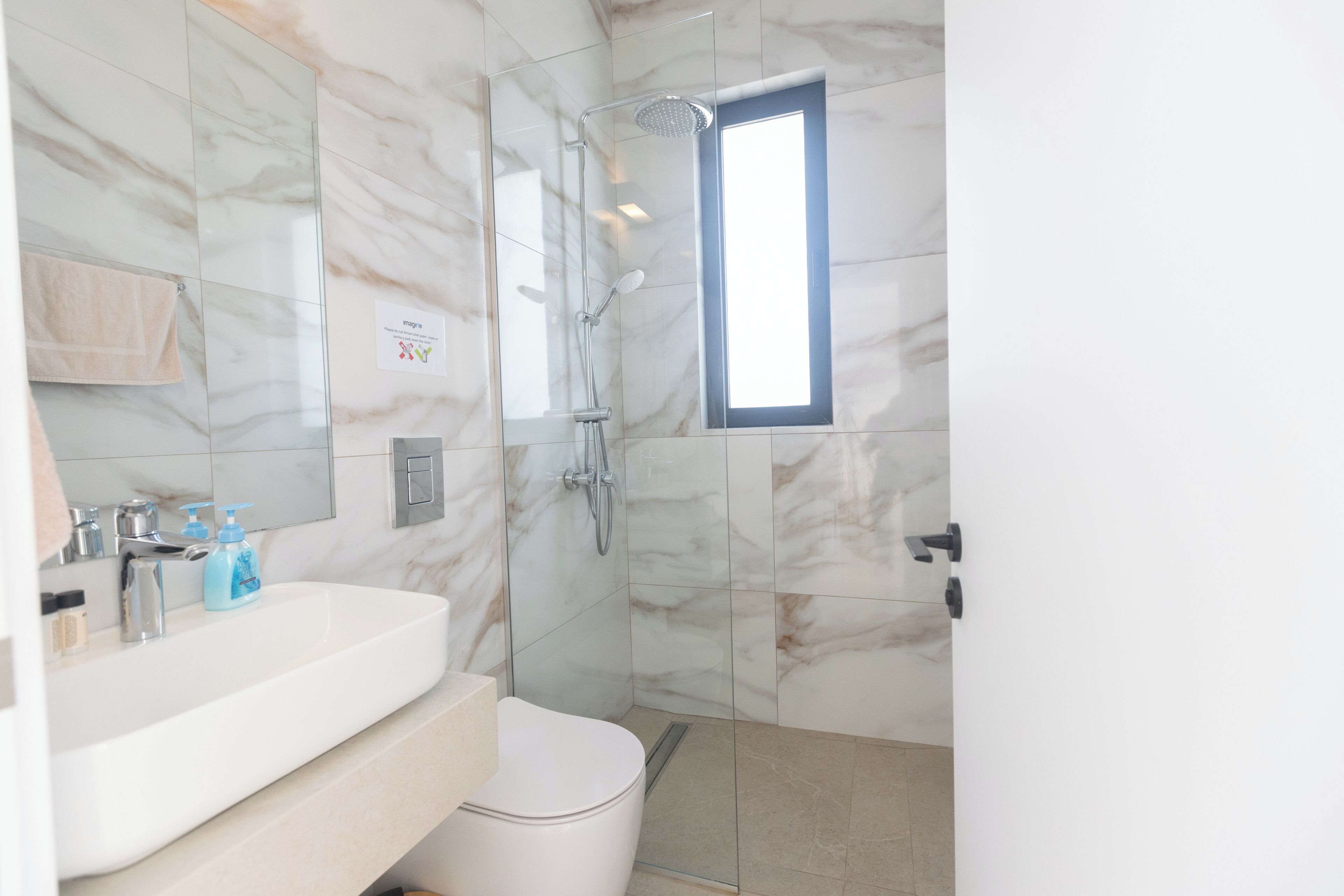 A bathroom with a marble wall, a white sink, a toilet, and a shower.